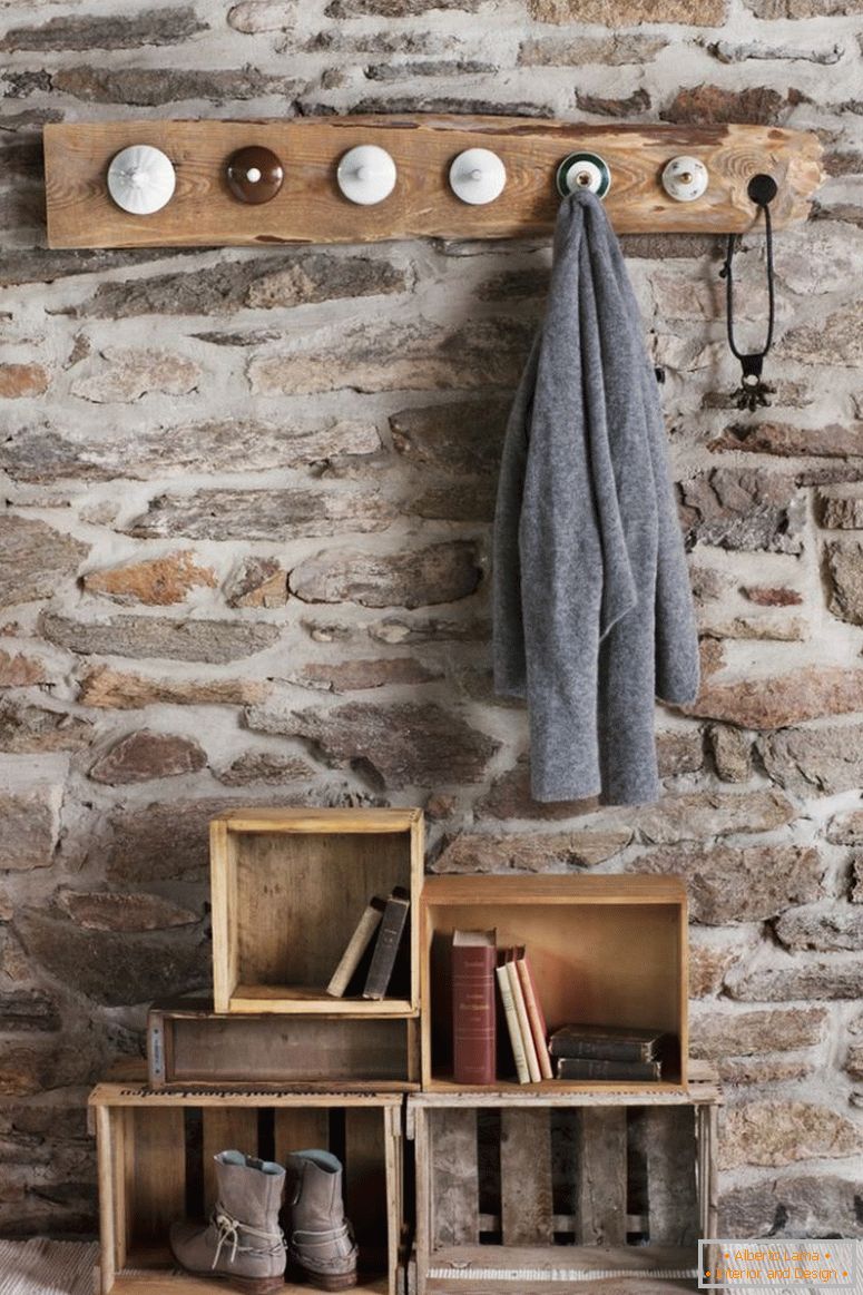 Rustic DIY garderoba u sobi sa kamenim zidom; šipke od kapuljača napravljene od starih poklopaca od kina i starih drvenih sanduka na podu kao skladištenje