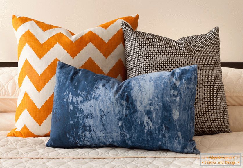 Svetle narandžaste, plave i crno-bele dekorativne jastuke sa zanimljivim otiscima na krevetu
